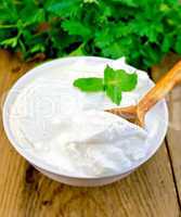 Yogurt in white bowl with mint and herbs on board