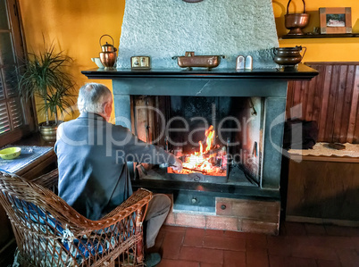 Retired man enjoying home warmth close to fireplace