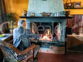 Retired man enjoying home warmth close to fireplace