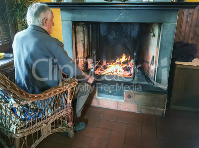 Retired man enjoying home warmth close to fireplace
