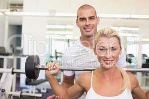 Trainer helping woman with lifting barbell in gym