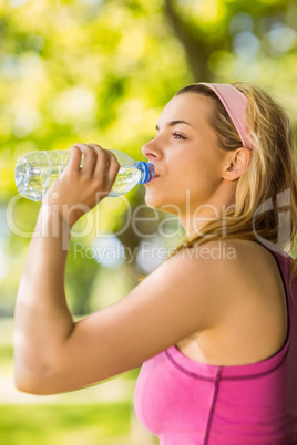 Fit blonde leaning against tree drinking water