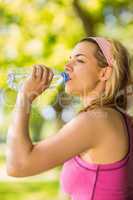 Fit blonde leaning against tree drinking water