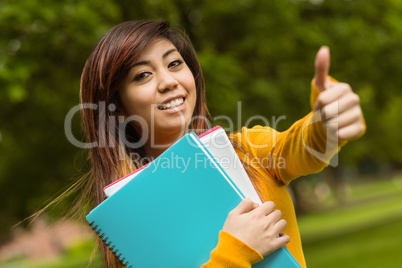 College student with books gesturing thumbs up in park