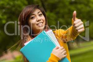 College student with books gesturing thumbs up in park