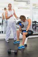 Male trainer assisting man with dumbbell in gym