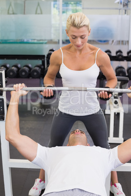 Trainer helping man with lifting barbell in gym