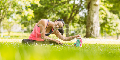 Smiling fit brunette stretching on the grass