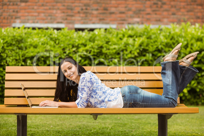 Peaceful brunette lying on bench using laptop