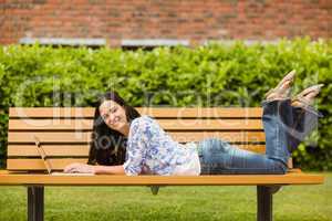 Peaceful brunette lying on bench using laptop