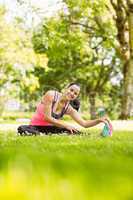 Happy fit brunette stretching on the grass