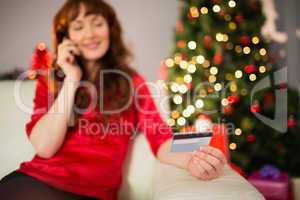 Smiling redhead phoning and holding credit card