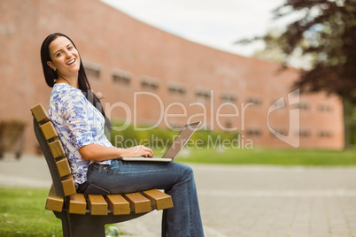 Happy brown hair sitting on bench using laptop