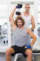 Trainer assisting young man with dumbbell in gym