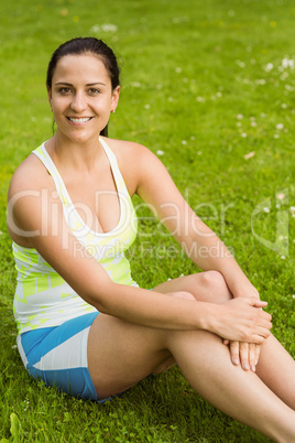 Happy fit brunette sitting on the grass