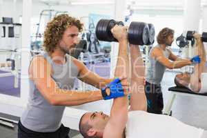 Male trainer assisting man with dumbbells in gym