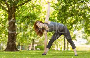 Pretty athletic redhead stretching in park