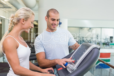 Trainer assisting woman with treadmill screen options at gym