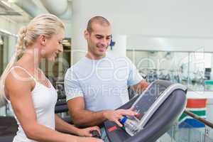 Trainer assisting woman with treadmill screen options at gym