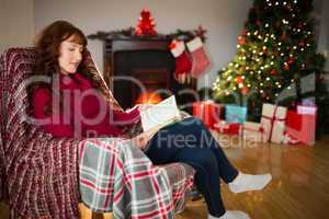 Smiling redhead reading on the armchair at christmas