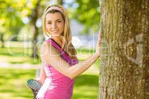 Fit blonde stretching against a tree