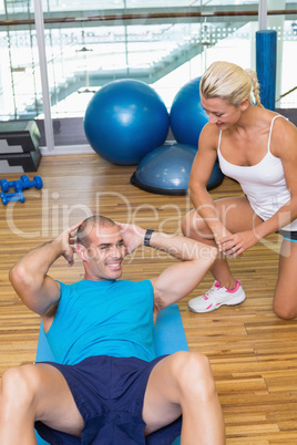Trainer assisting man with abdominal crunches at fitness studio