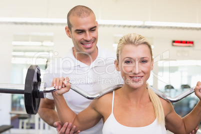 Trainer helping woman with lifting barbell in gym