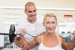 Trainer helping woman with lifting barbell in gym