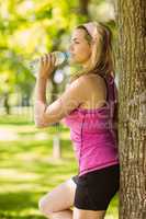 Fit blonde leaning against tree drinking water