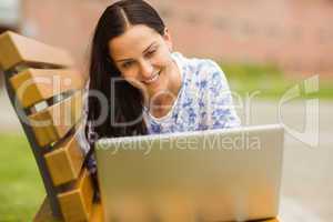 Smiling brunette lying on bench using laptop