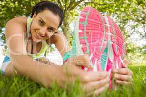Smiling athletic brunette stretching on the grass