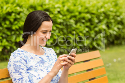 Cheerful brunette sitting on bench texting