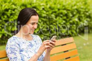 Cheerful brunette sitting on bench texting