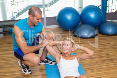 Trainer assisting woman with abdominal crunches at fitness studi