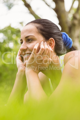 Smiling fit brunette relaxing and thinking on grass