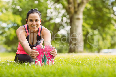 Cheerful fit brunette stretching on the grass