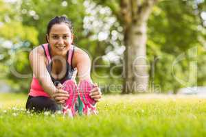 Cheerful fit brunette stretching on the grass