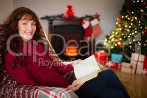 Cheerful redhead reading on the armchair at christmas