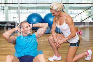 Trainer assisting man with abdominal crunches at fitness studio