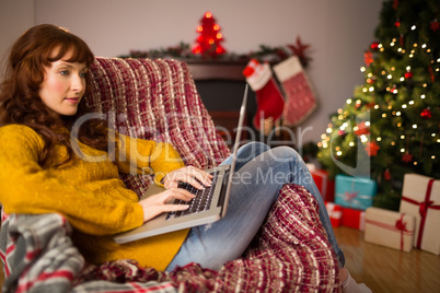 Redhead woman sitting on couch using laptop at christmas