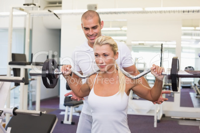 Trainer helping woman with lifting barbell in gym