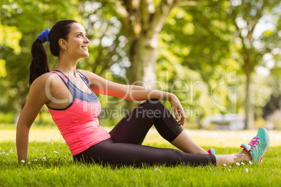 Cheerful fit brunette day dreaming on the grass