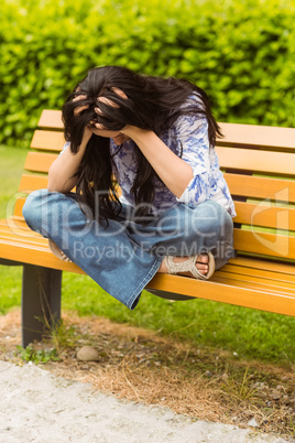Brunette sitting on bench holding her head