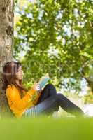 Female college reading book against tree trunk in park