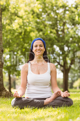 Smiling brunette in lotus pose on grass