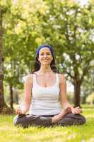 Smiling brunette in lotus pose on grass