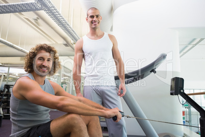 Male trainer assisting man on fitness machine at gym