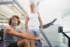 Male trainer assisting man on fitness machine at gym