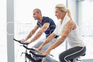 Determined couple working on exercise bikes at gym
