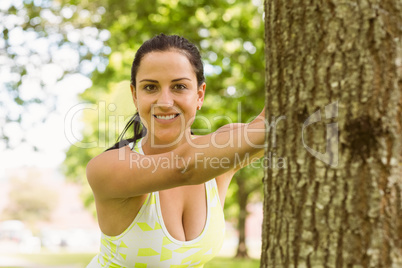 Happy fit brunette stretching against a tree